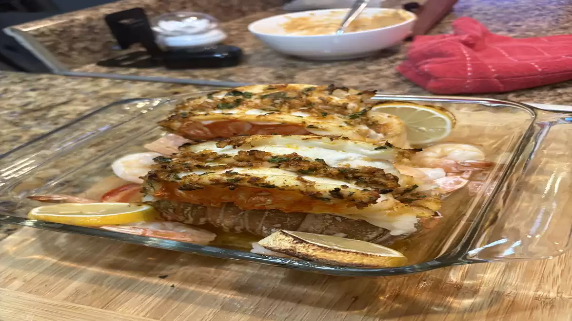 Delicious preparation of herb-crusted lobster pieces served on a glass dish with lemon slices on a kitchen table.