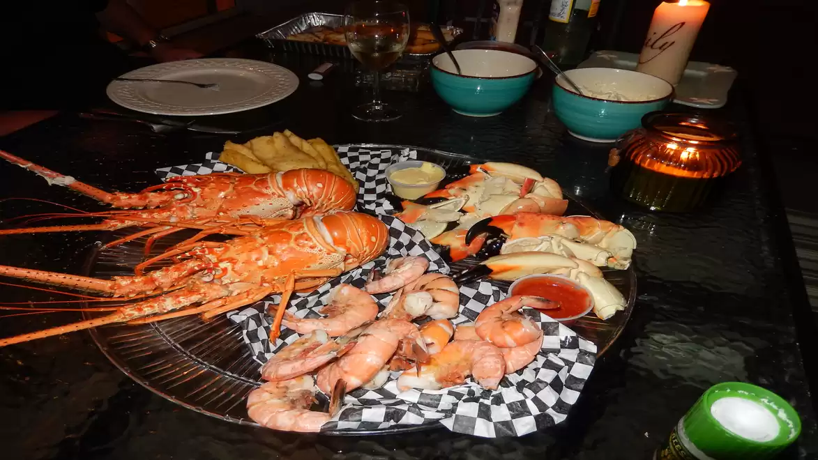 A plate with a selection of seafood, including large lobsters and shrimp, served on black-and-white checkered paper. In the background are bowls and a candle on a table.
