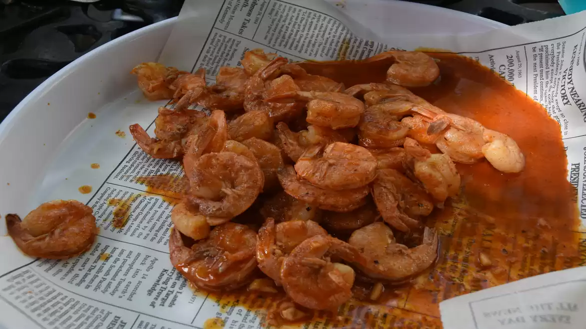 A plate of fried shrimp in a spicy red sauce, served on newspaper.