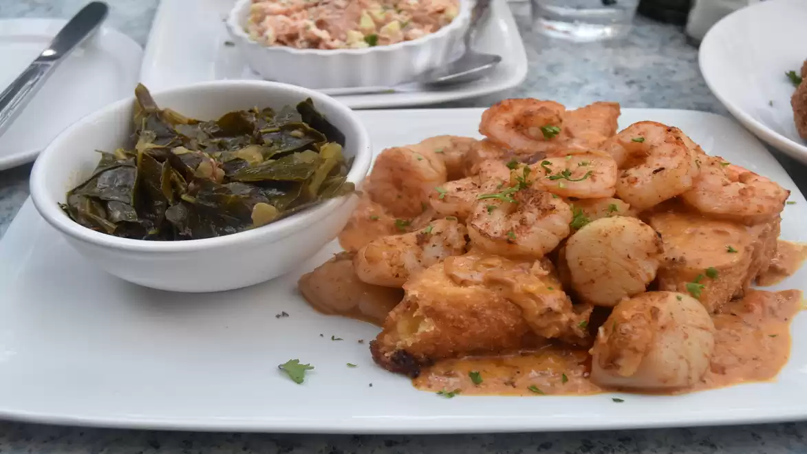 A plate of fried shrimp in a spicy sauce, served with a side of green leafy vegetables.