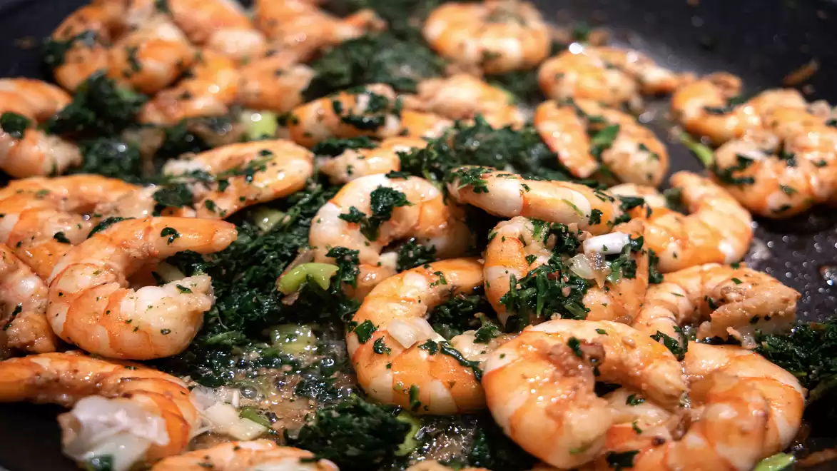 Fried shrimp with chopped spinach in a pan, seasoned with fresh herbs and garlic.