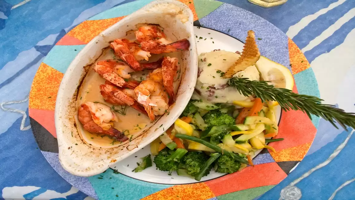 A colorful dish with grilled shrimp in a white dish, accompanied by mixed vegetables and a decorative rosemary sprig.