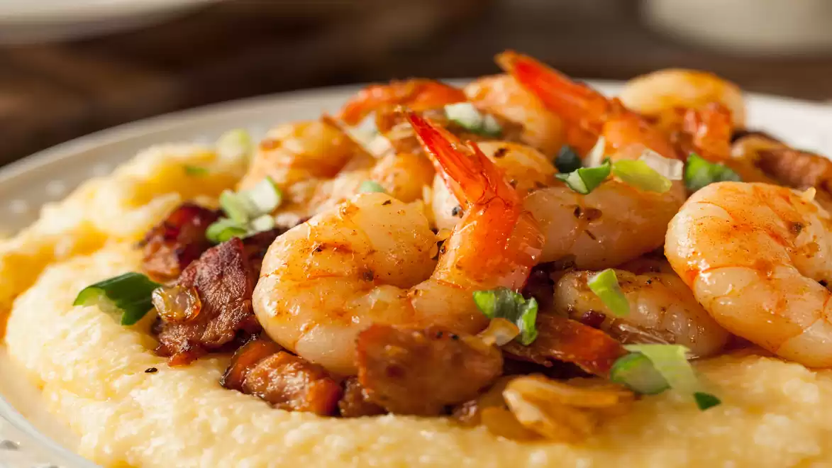 A plate of creamy grits topped with juicy shrimp and fresh herbs.
