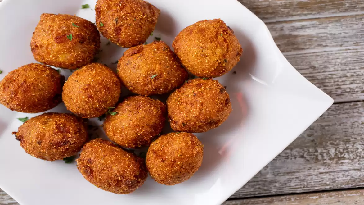 A plate of crispy, golden-brown Hush Puppies on a wooden background.