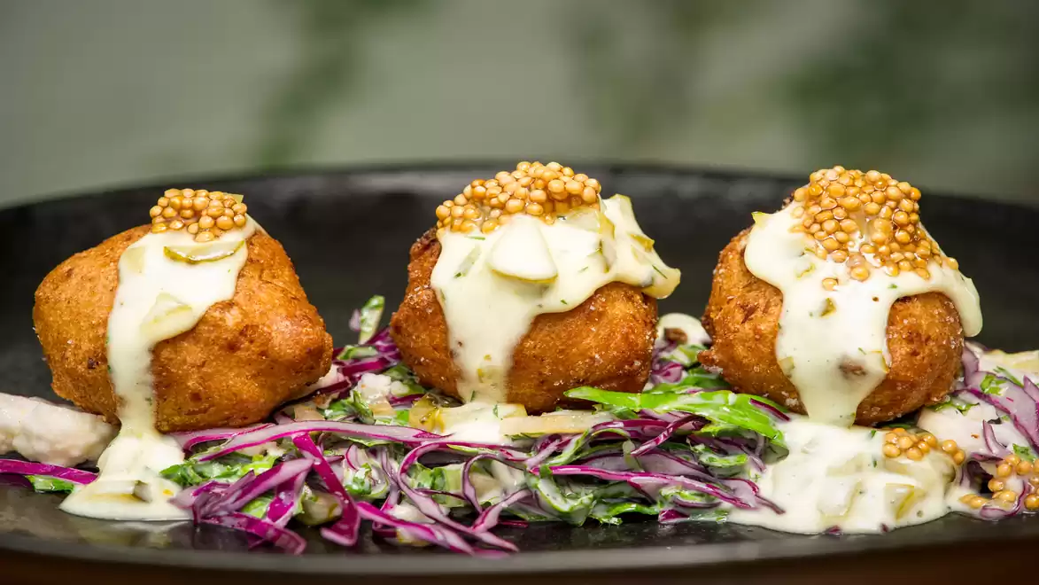 Three fried Hush Puppies with mustard sauce served on a bed of colorful coleslaw.