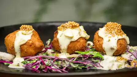 Three fried Hush Puppies with mustard sauce served on a bed of colorful coleslaw.