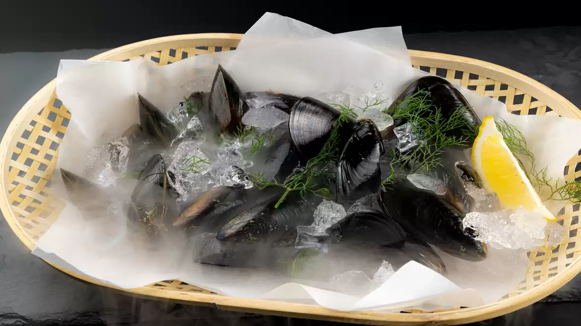 Fresh mussels on ice in a basket with lemon wedge and dill.