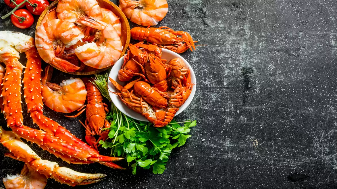 Fresh seafood assortment on black background with shrimp, crabs, and herbs.