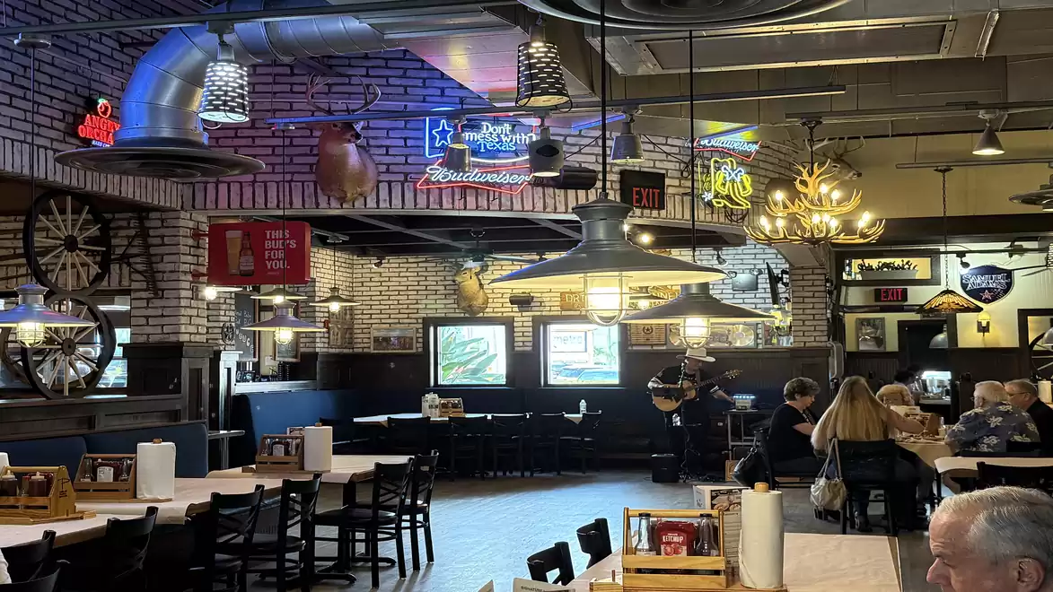 Interior of a cozy restaurant with brick walls, neon lights, and rustic decor. People are sitting at tables enjoying their meal.