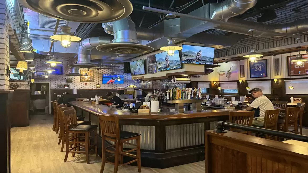 A cozy sports bar interior with wooden furniture, TVs on the walls showing sports events, and a large bar in the center.
