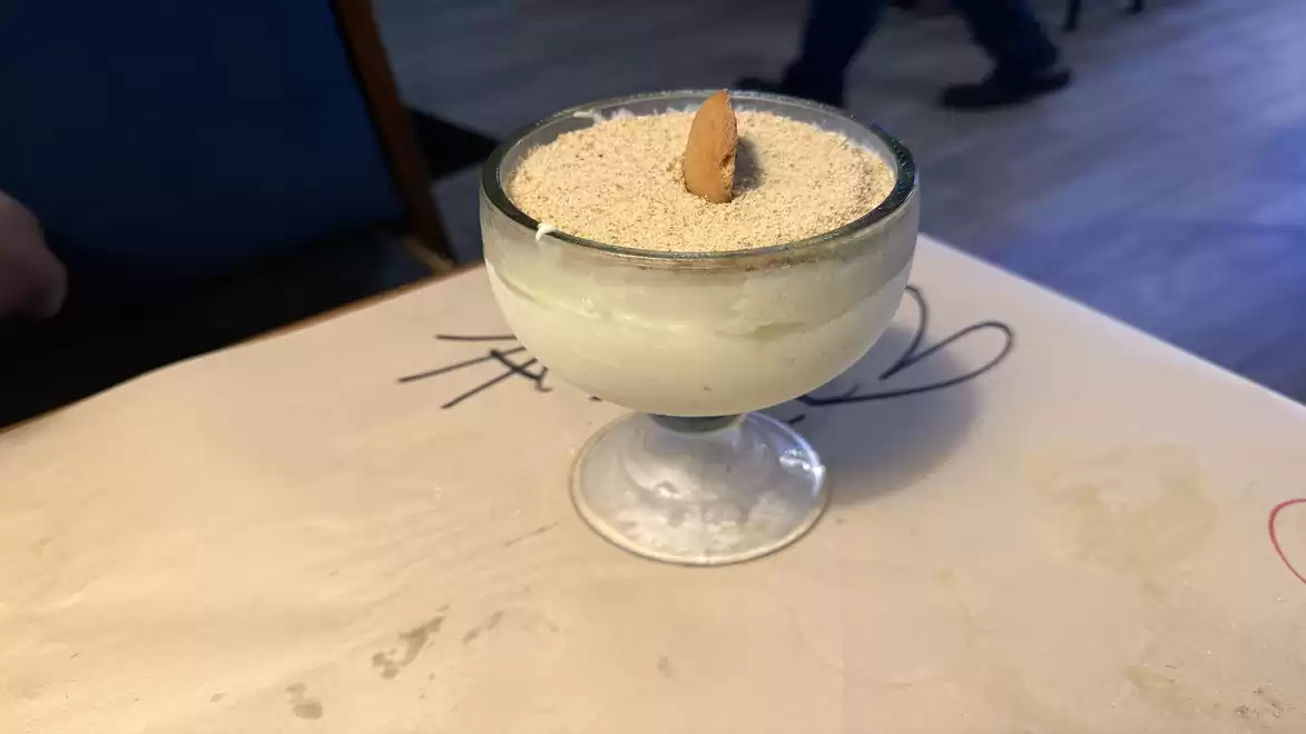 A dessert in a glass, sprinkled with ground nuts and topped with an almond, served on a table.