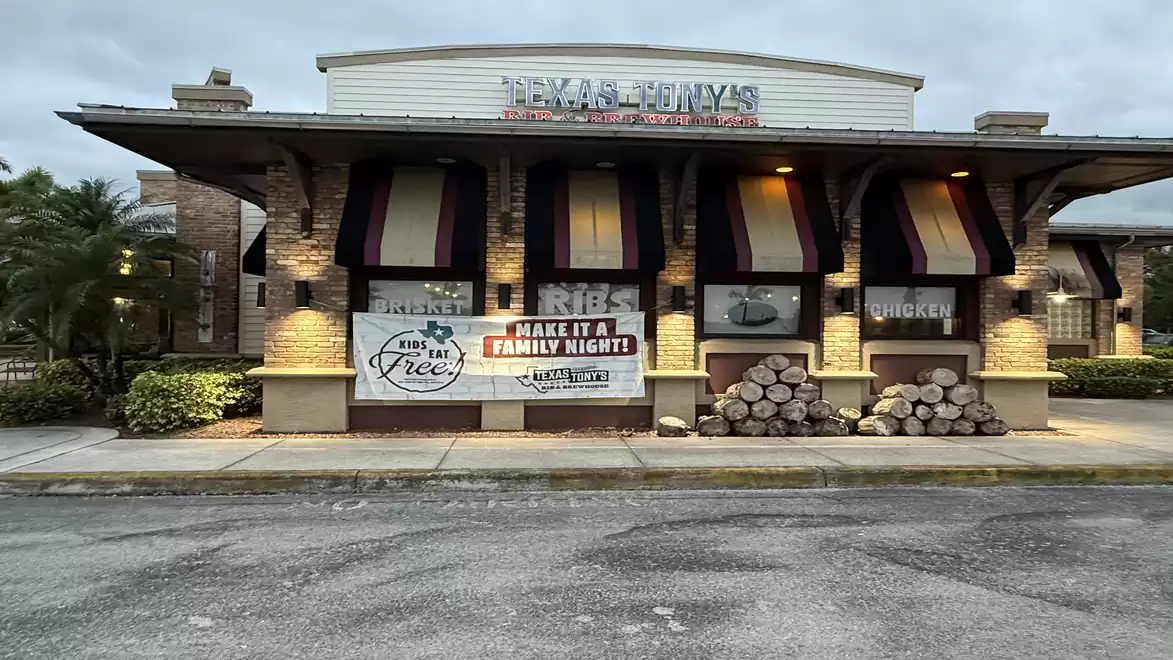 Exterior view of a restaurant with wood stacks in front and illuminated facade, signs advertising ribs and family nights.