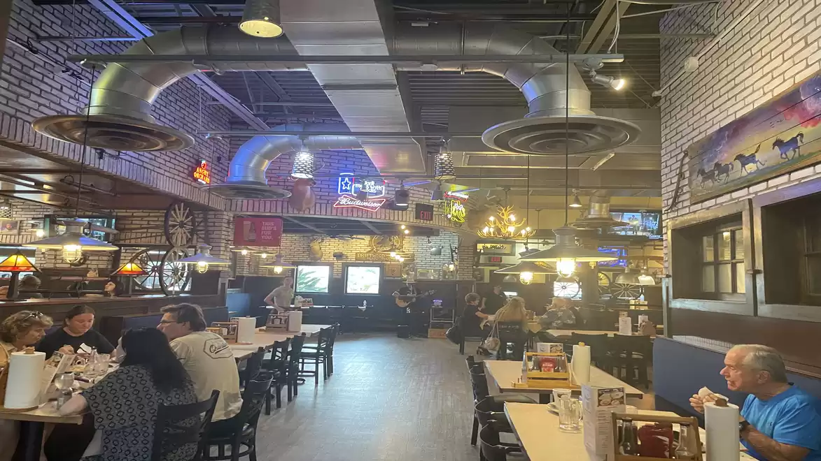 Interior view of a bustling restaurant with many guests at wooden tables, colorful neon lights hanging from the ceiling in an industrial setting.