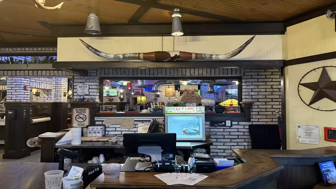 Interior view of a restaurant with rustic decor, including a horn mount on the wall and a computer at the counter.