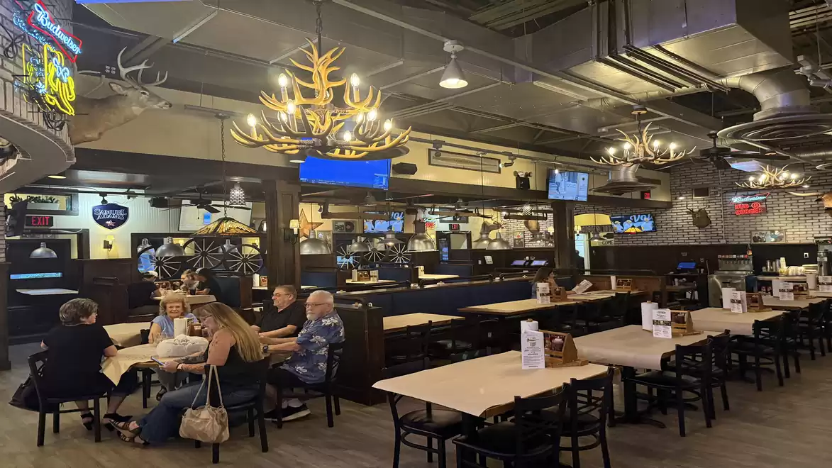 Interior view of a restaurant with warm lighting design, featuring multiple tables and seating areas. A group of people is seated at a table.