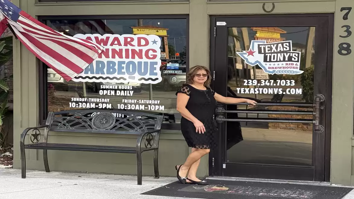 Woman in a black dress in front of a barbecue restaurant with US flag and signs.