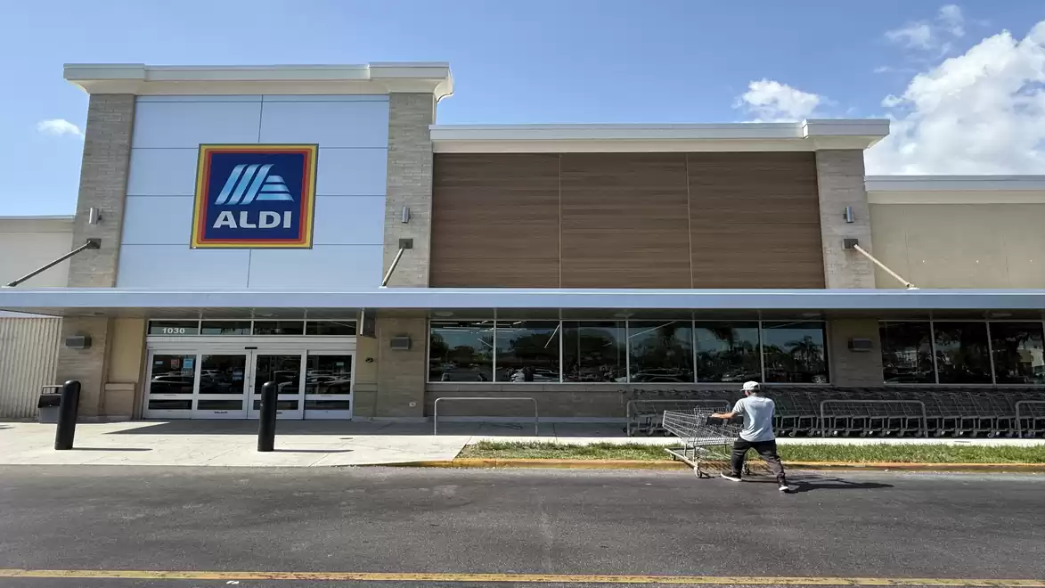 ALDI supermarket with parking spaces and a customer with a shopping cart in the foreground.