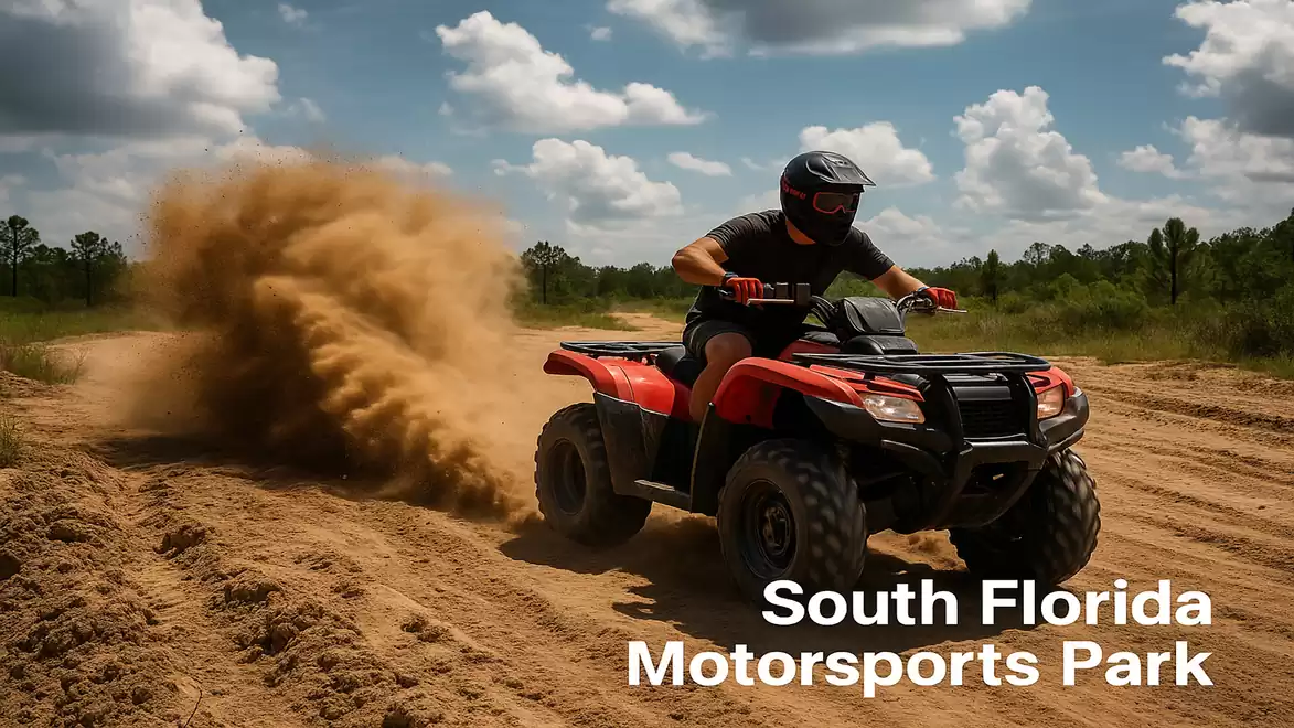 A man rides a red ATV on a dusty off-road track in South Florida Motorsports Park under a blue sky with clouds.