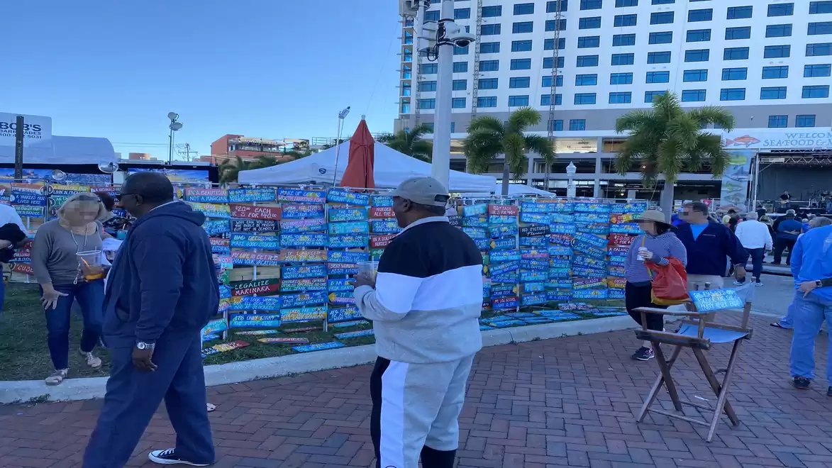 People strolling at an outdoor market in front of a high-rise building, surrounded by postcards and stalls.