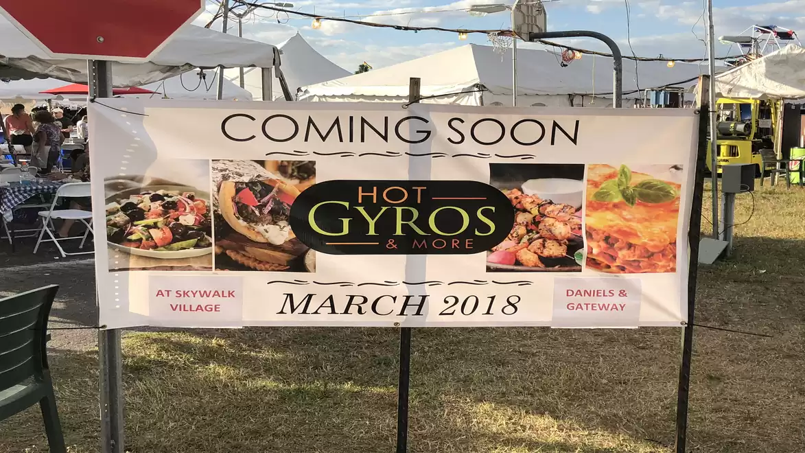 An advertising banner at a market announces the opening of a new restaurant called 'Hot Gyros & More' for March 2018. There are food images and the text 'Coming Soon'.