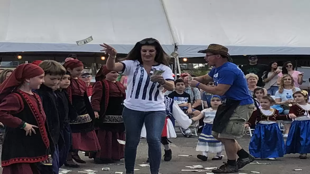 A woman dances joyfully among a group of traditionally dressed children at a cultural festival.