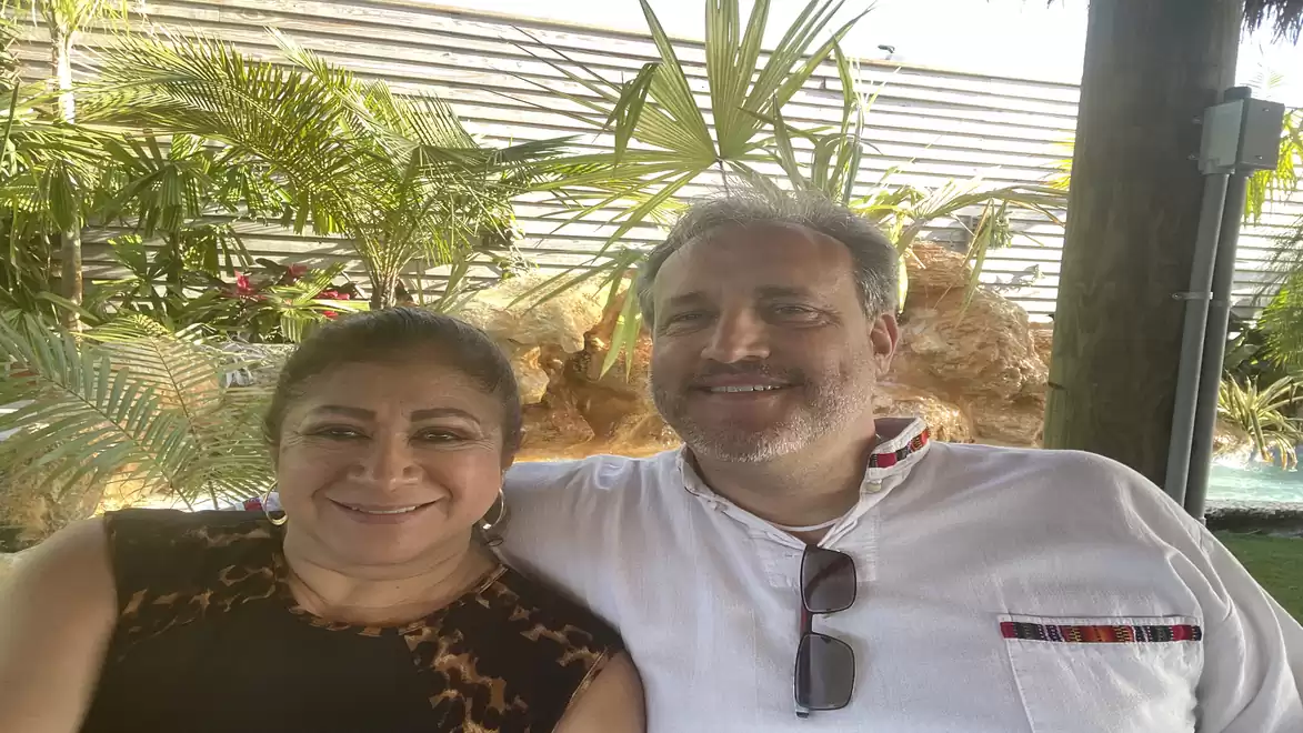 A smiling couple relaxing in a tropical garden with green plants in the background.