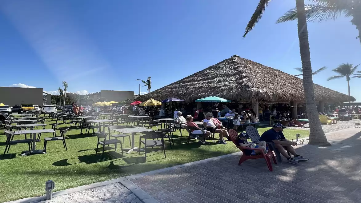 Outdoor scene with a thatched-roof pavilion, people relaxing under the blue sky.