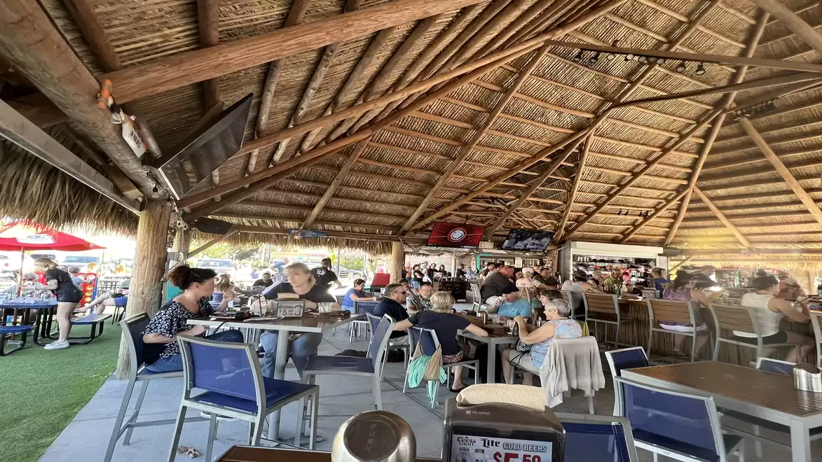 A covered restaurant with a thatched roof, where many people are sitting at tables eating.
