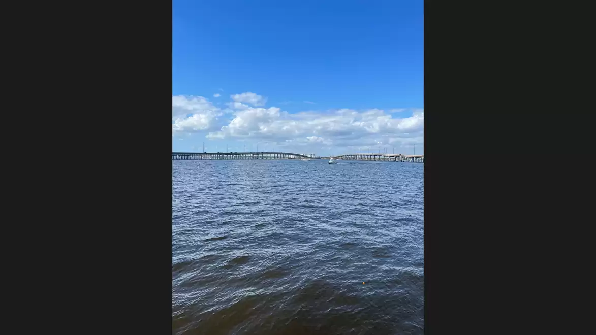 View of a body of water with a bridge in the background under a blue sky with white clouds.