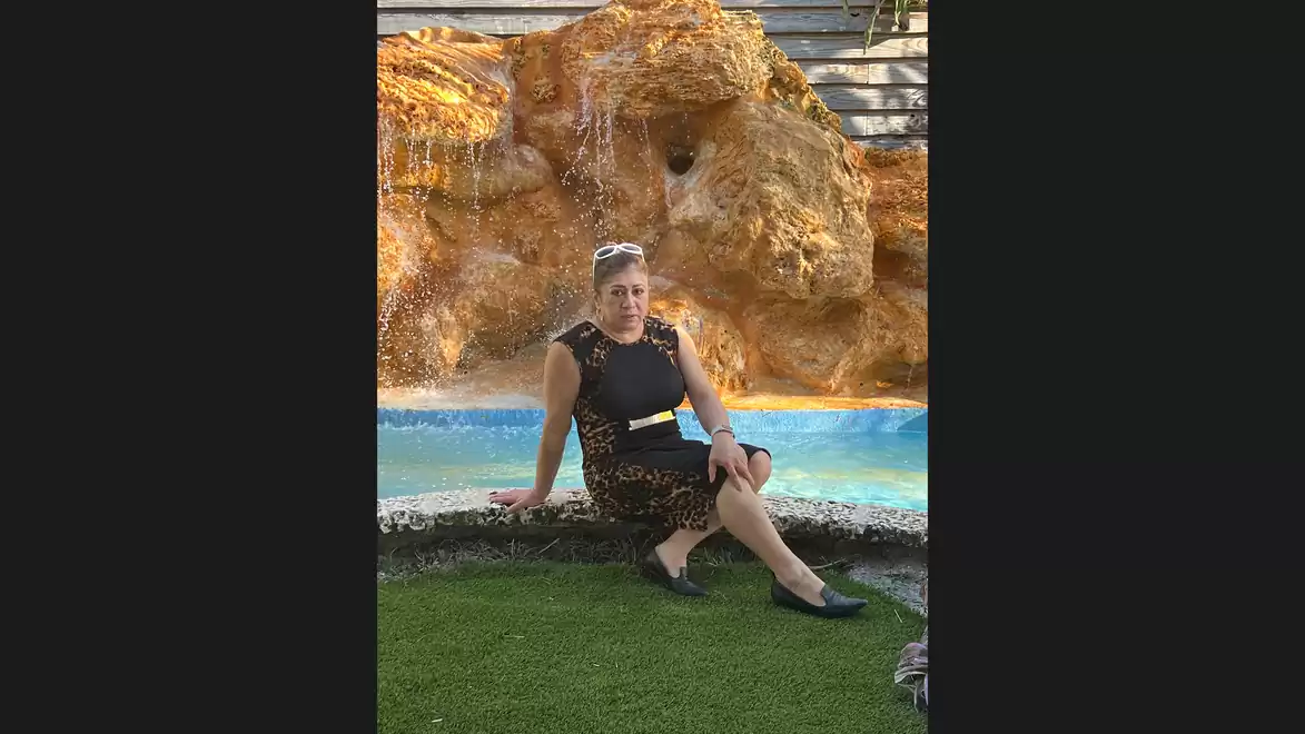A woman sits in a black dress in front of an artificial waterfall.
