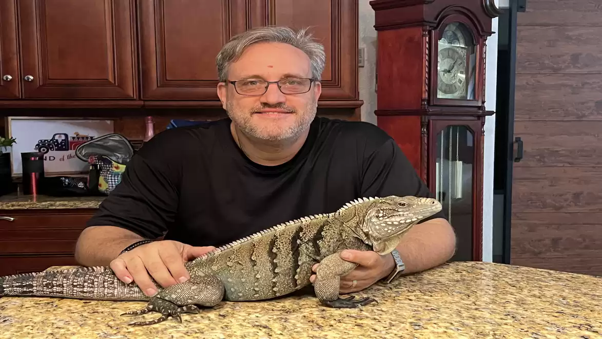 A man sits at a kitchen table holding a large lizard.
