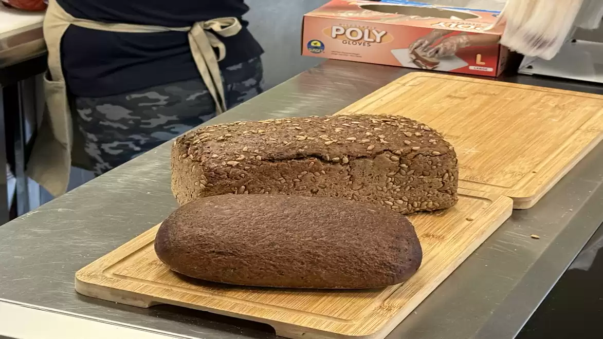 Two freshly baked loaves on a wooden board, one lighter multigrain bread and one dark rye bread.