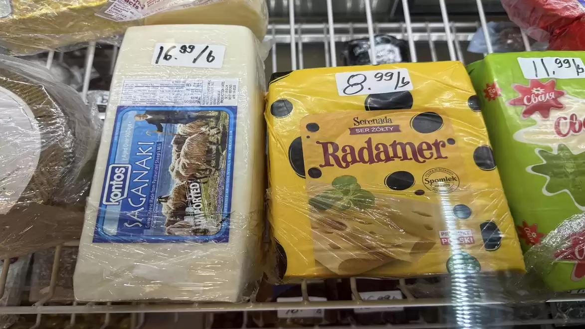 A close-up of various types of cheese on a supermarket shelf with price tags.