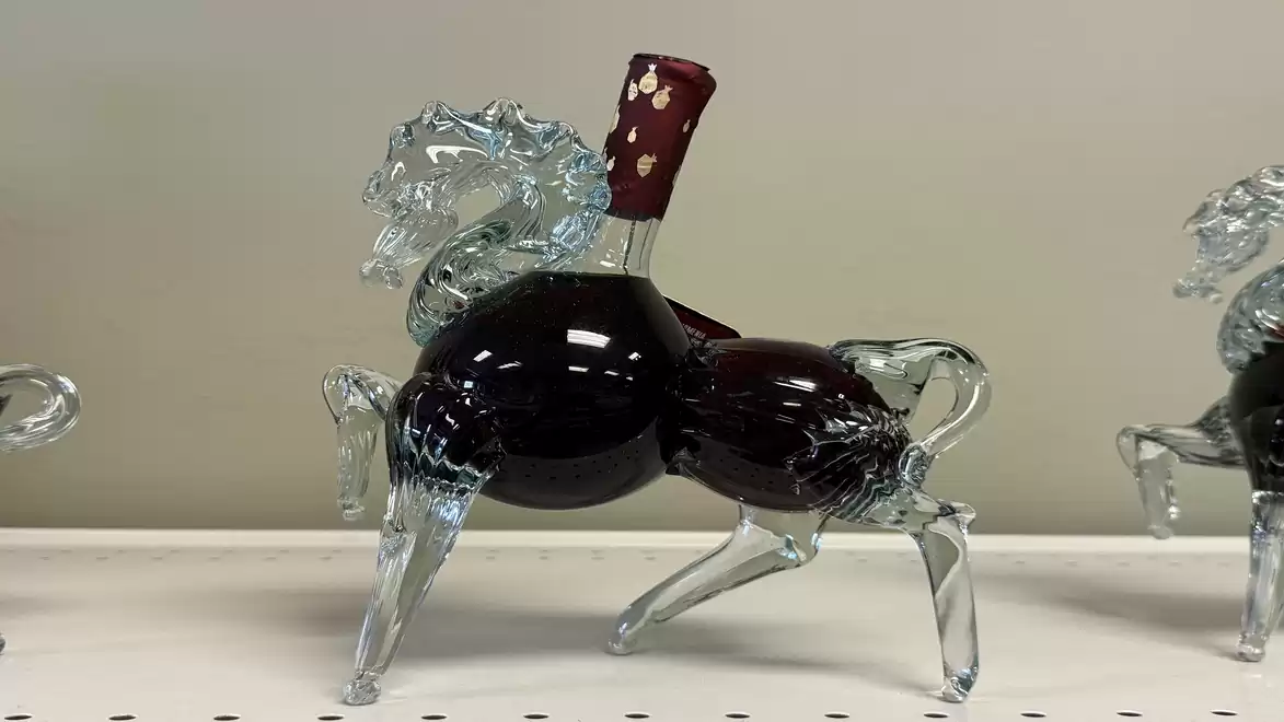 Image of a glass vessel shaped like a horse filled with red wine.