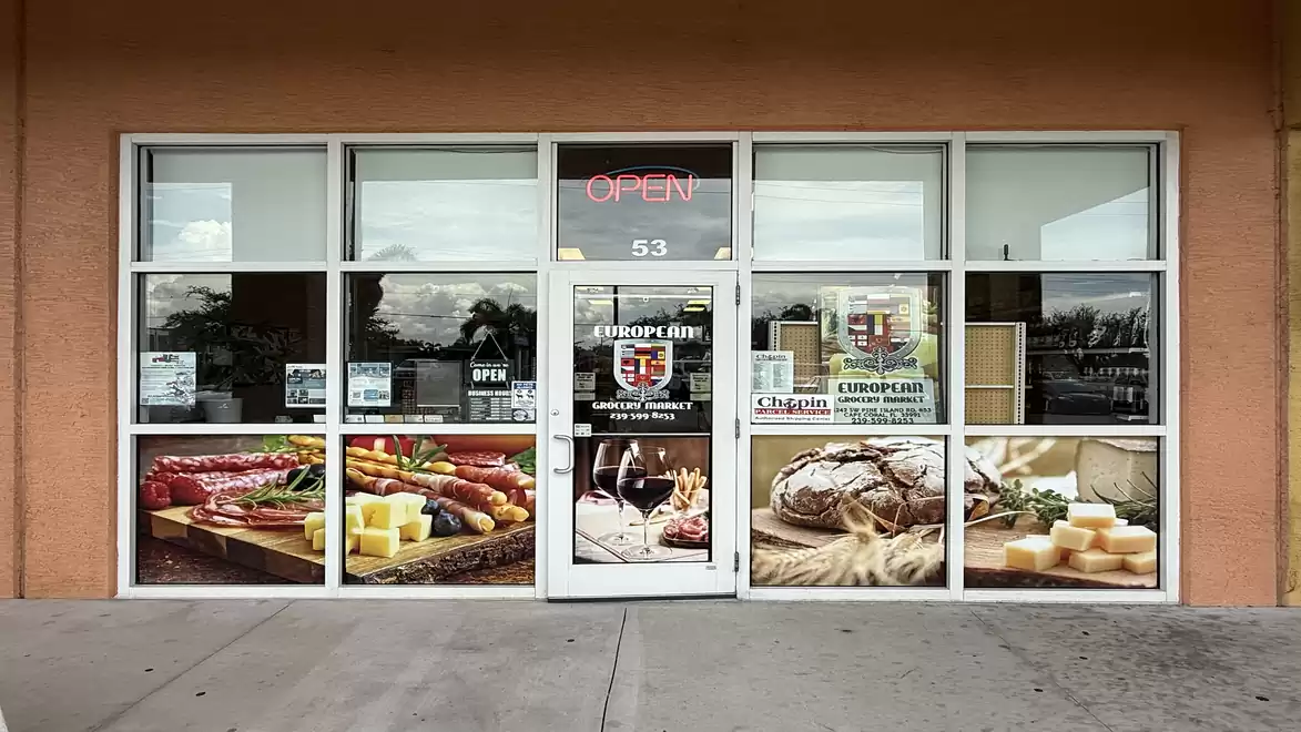 Front entrance of a European deli with images of sausages, bread, and cheese in the windows.