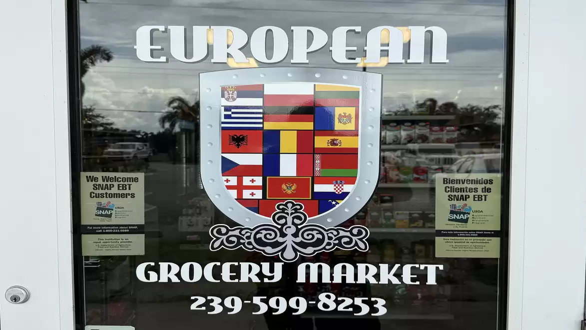 Entrance of a European grocery market featuring a sign with various European national flags.