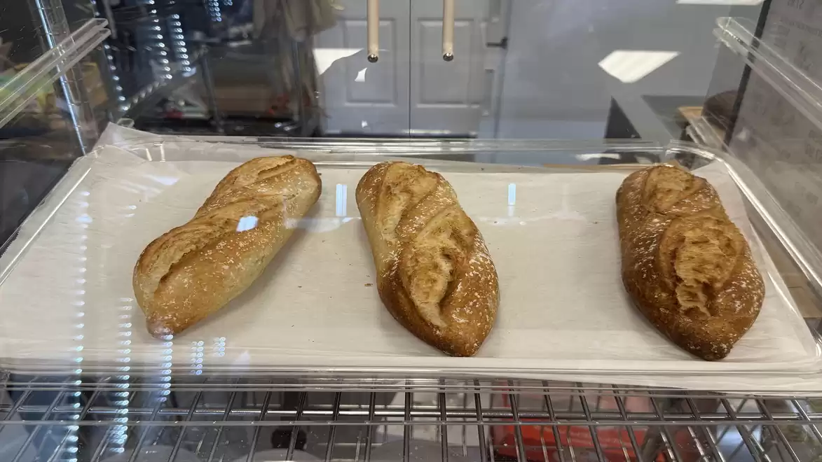 Three freshly baked, golden-brown baguettes on a tray in a bakery display.
