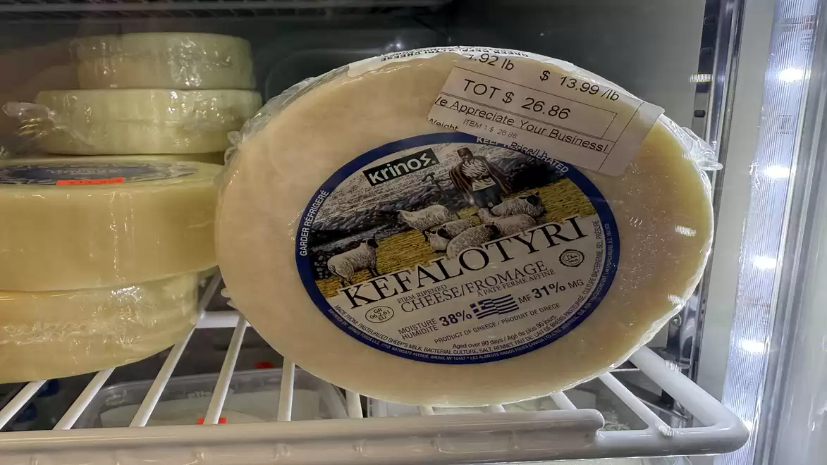 A round loaf of Kefalotyri cheese in a refrigerated display, with a price tag and fat content information.