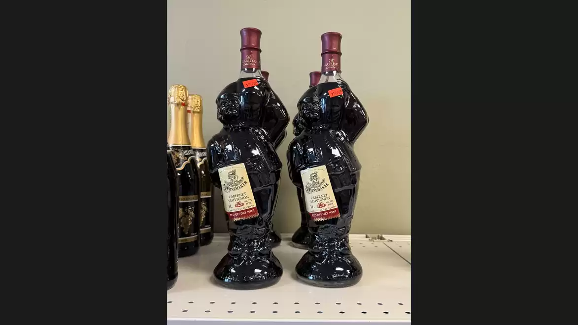 Several bottles of red wine shaped like bears stand on a shelf. Some champagne bottles are visible in the background.