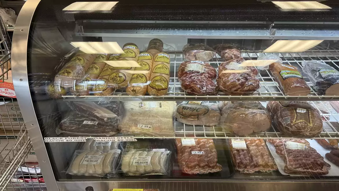 A refrigerated display case in a supermarket shows various packaged foods like bread, sausages, and cold cuts.