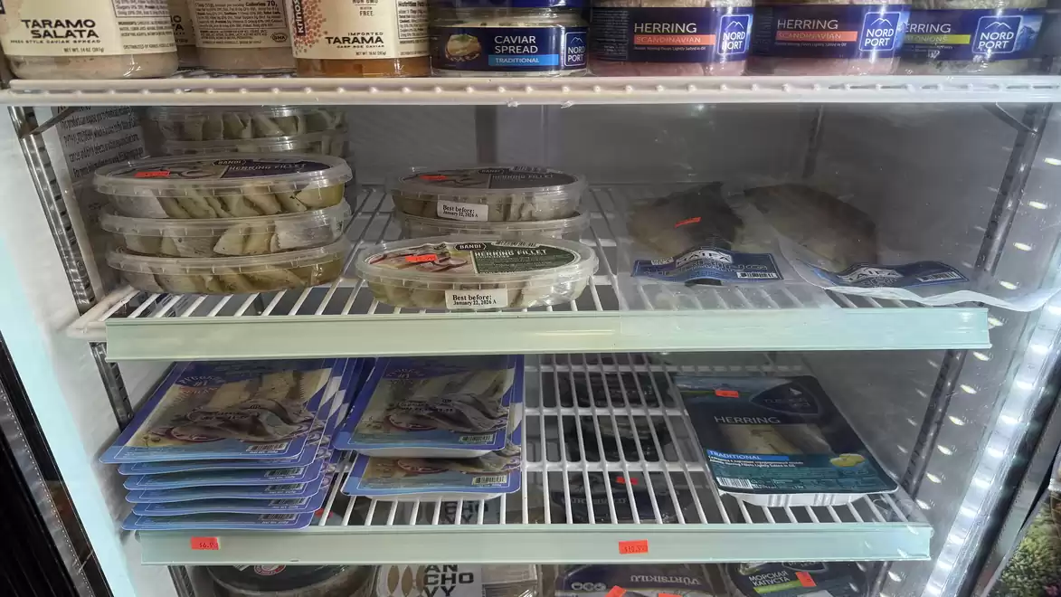 Refrigerated shelf with various packaged seafood and herring in a store.