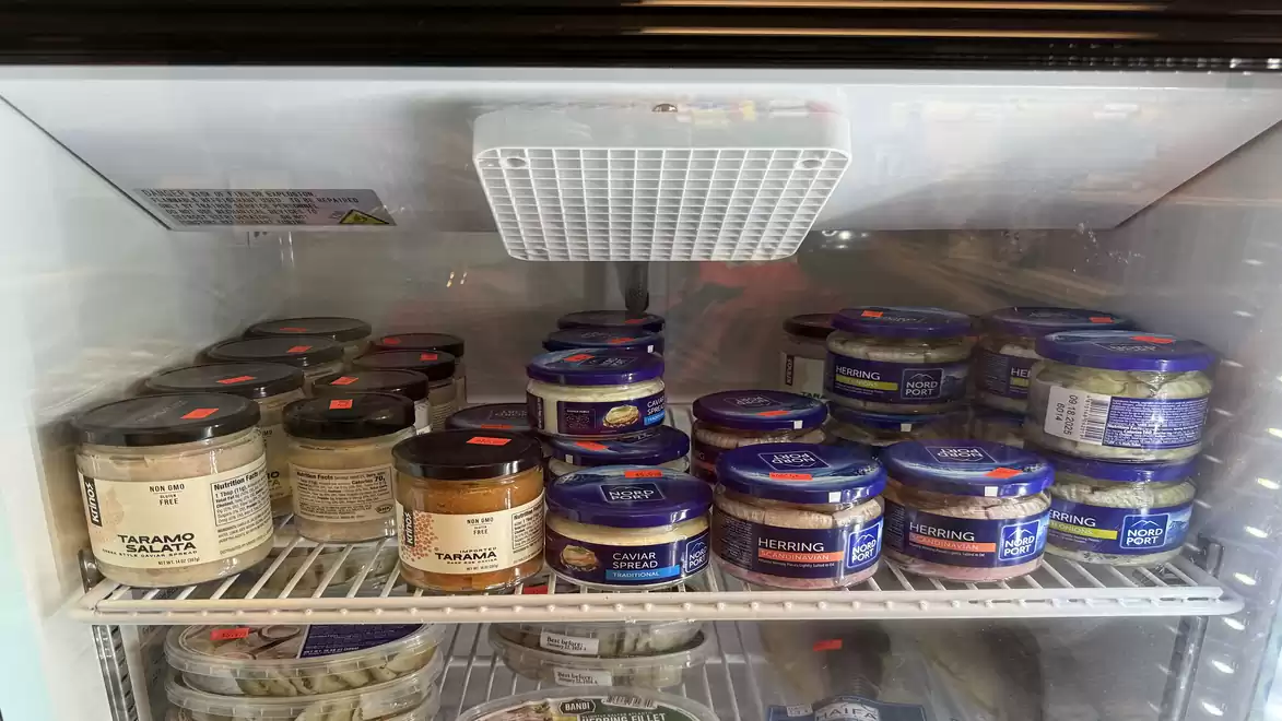 A refrigerator containing various tins of fish roe, including caviar, with blue and black labels.