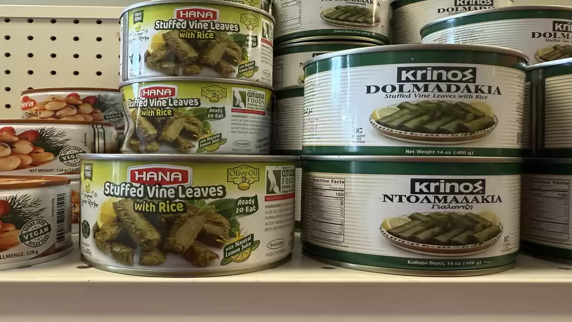 Shelf with cans of stuffed vine leaves by HANA and Krinos in a store.