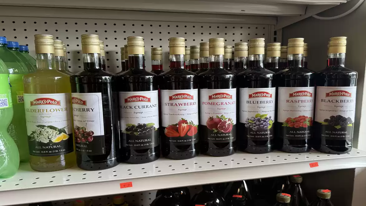 Shelf with various bottles of fruit syrups featuring flavors like elderflower, cherry, black currant, and strawberry in a store.