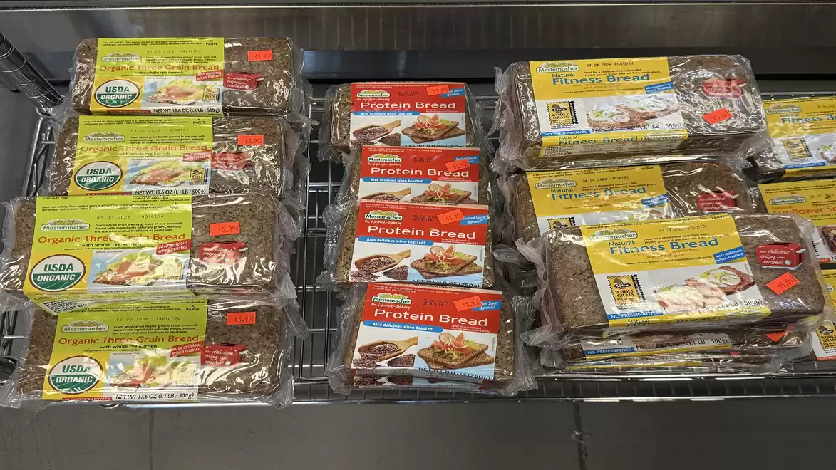 Shelf with various types of packaged whole grain and protein bread in the supermarket.