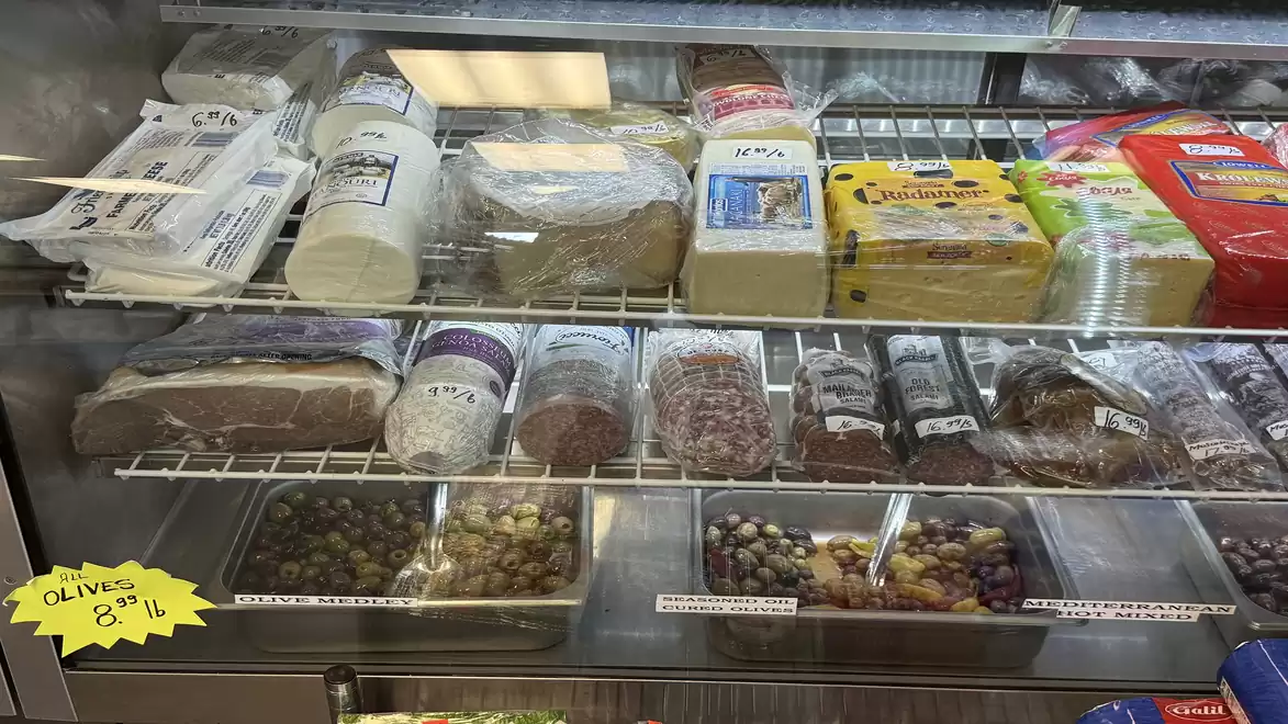 A refrigerator filled with various types of cheese and olives in a store.