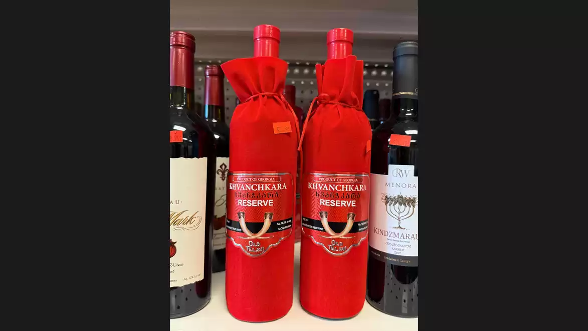 Shelf with various wine bottles, including noticeable red bottles of Khvanchkara Reserve in the center.