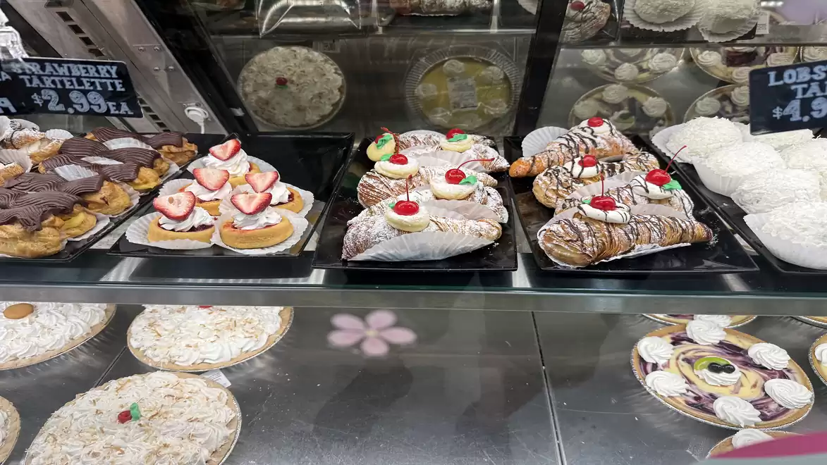 A bakery display featuring various pastries, including fruit tarts, cream cakes, and powdered sugar pastries decorated with cherries.