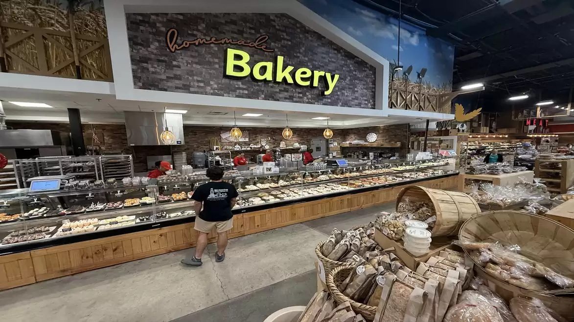 A large bakery shop with a wide variety of baked goods, a customer stands in front of the long counter.