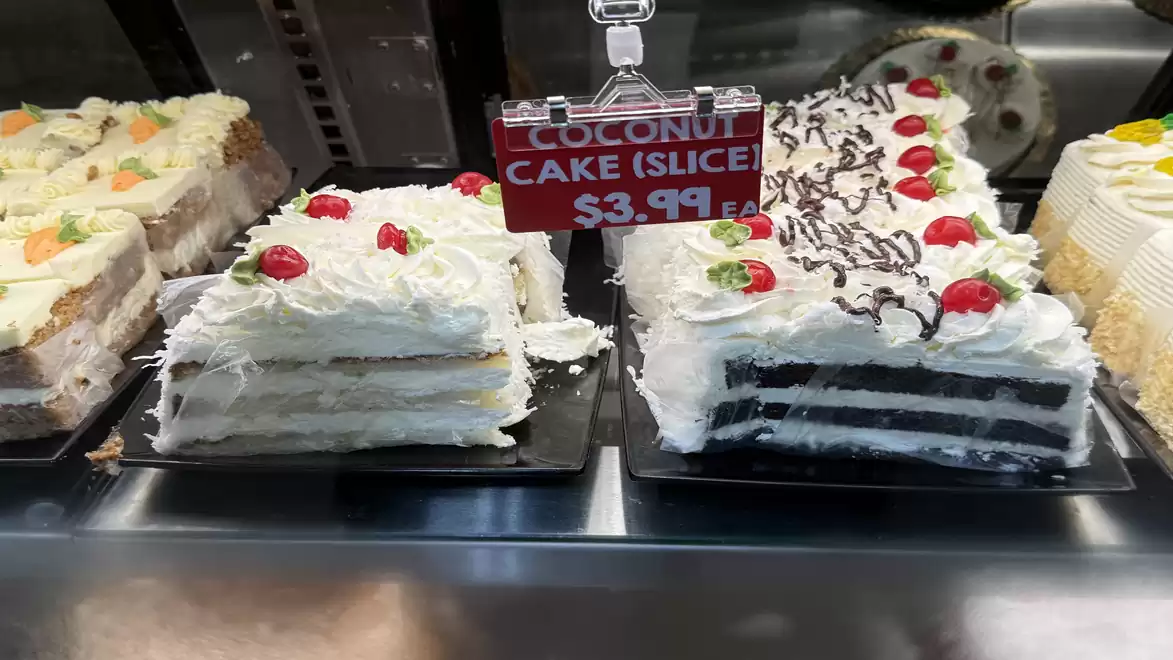 A selection of cake slices with white frosting and cherries in a bakery display, with a price tag of $3.99.